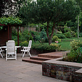 Klinker-Terrasse mit Stufen zum Garten mit mediterranen Pflanzen. Vitis vinifera (Weinrebe), Pinus 'Brant & Umbrella Pine' (Schirmkiefer)