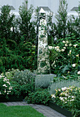Obelisk mit Spiegelseiten in weißem Beet mit Rosen, Lilien und Digitalis (Fingerhut)