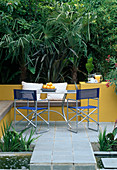 Sitzplatz: Aluminiumtisch und Stühle auf Innenhof, Trachycarpus, gelbe Mauer mit eingebauter Bank