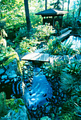 Ein Wasserfall stürzt einen Hügel hinunter in den Koiteich mit einem indonesischen Pavillon daneben im Wald