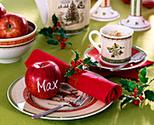 Ilex 'Alaska' / Stechpalme, Malus / Äpfel, rote Serviette, Weihnachtsgeschirr.