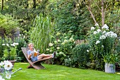 Lesende Frau auf Holzliegestuhl in gepflegtem Garten