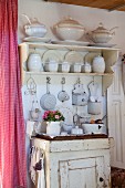 White crockery on wall-mounted shelves and kitchen utensils on old cabinet