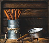 Cinnamon sticks in a tin tied with string, anise stars and a sieve on a rustic wooden background