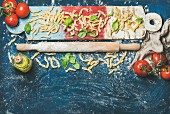 Fresh pasta casarecce, tomatoes, basil leaves and bottle of olive oil on colorful painted wooden board