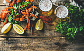 Two glasses of wheat beer and boiled crayfish in a pan served with lemon and parsley on a rustic wooden table