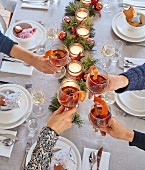 Hands raising glasses of mulled wine over a festively set dining table