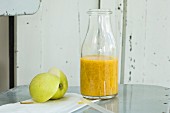 A mango and orange smoothie with chia seeds in a bottle on an old chair with an apple