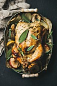 Oven roasted whole chicken with onion, apples and sage leaves in serving tray