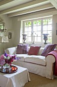 Scatter cushions on loose-covered sofa below lattice window in country-house interior