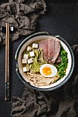 Bowl of asian style soup with green tea soba noodles, beef, egg, mushrooms, spring onion and tofu cheese