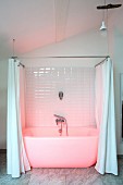 White bathtub with shower curtain bathed in pink light in renovated period building