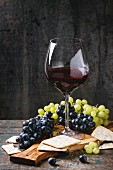 Bunches of ripe wet red and white grapes with crackers snack and glass of red wine on olive wood cutting board