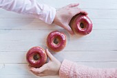 Zwei Hände greifen nach rosa glasierte Doughnuts