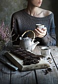 Frau trinkt Tee, im Vordergrund dunkle Schokolade