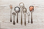 Seven vintage spoons of diffrent types of salt on a white wooden surface