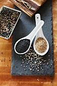 Black and white sesame seeds in spoons on a slate plate