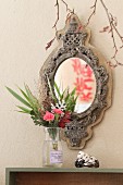 Oriental lantern with red lettering reflected in mirror with carved wooden frame above vase and shell on shelf with