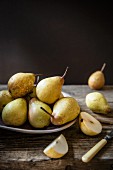 Pears on a plate, some sliced, against dark background
