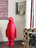 Red plastic penguin in front of modern artwork in corner of room