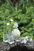 Verschiedene weiße Blumen in Glasväschen auf einem Steintrog