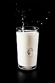 A glass of milk with a splash on a black background