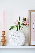 Turned candlesticks, pink candle and speckled vase of flowers on wall-mounted shelf