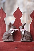 Two chocolate bunnies with pink ribbons on red picket fence