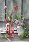Vintage-style arrangement of stacked zinc pots, snake's head fritillaries in glass vases and sprigs of rosemary