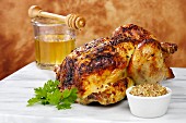 A whole cooked roast chicken with a honey and mustard glaze, showing a dish of mustard and a honey jar and honey drizzler