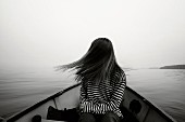 A young girl wearing a striped top sitting in a boat and tossing her hair to the side (black and white photo)