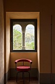 Chair with red upholstery in niche below Romanesque window with stone pillar