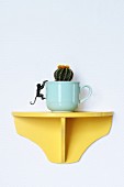Cactus planted in cup on yellow wall bracket