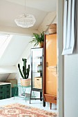 Various retro furnishings and house plants below sloping ceiling