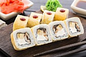 Sushi-Rollen mit geräuchertem Aal und Banane auf einem Holzbrett