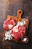 Raw fresh cross cut veal shank and Ingredients for making Osso Buco on wooden cutting board on dark wooden background