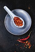 Assortment of dryed whole and flakes red hot chili peppers in ceramic spoon over black background