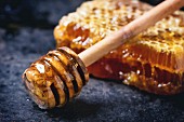 Honeycomb with honey dipper over black surface