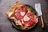 Raw fresh cross cut veal shank for making Osso Buco on metal copper plate on wooden background with meat cleaver