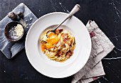Pasta Carbonara on white plate with parmesan and yolk on black marble background