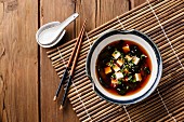 Miso-Suppe mit Tofu, Algen und Sesam in einer Schüssel auf Bambusset