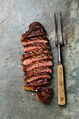 Sliced grilled beef barbecue Striploin steak and meat fork on gray stone slate background