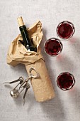 A packed wine bottle, glasses of red wine, and a corkscrew