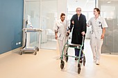 Nurses helping senior male to walk corridor