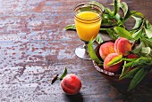 Peaches on branch with leaves in wooden bowl and glass with peach s juice over old metal background