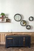 Round mirrors above modern sideboard against wainscoting