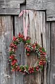 Romantic heart-shaped wreath of rose hips and moss hung on rustic board wall