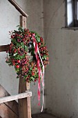 Herbstkranz mit Hagebutten, Moos und rot-weissen Schleifenbändern an Treppenpfosten von Vintage Holzstiege