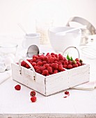A still life with fresh raspberries in a wooden crate, and pastry utensils in the background