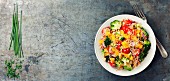 Quinoasalat mit Brokkoli, Paprika, Karotten, Zwiebeln und Tomaten auf rustikalem Metalluntergrund